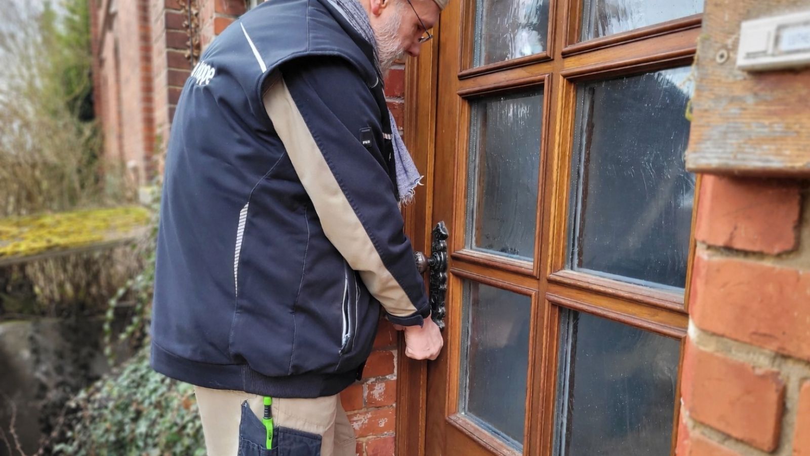 Tischlermeister Hoppe öffnet mit einem Schlüsseldienst-Werkzeug eine Haustür.